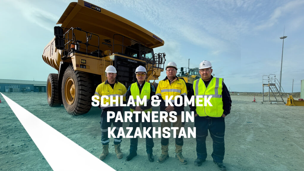 "Four workers in high-vis vests and hard hats stand in front of a Komatsu HD785 haul truck fitted with a Schlam Hercules truck bed at a mine site in Kazakhstan."