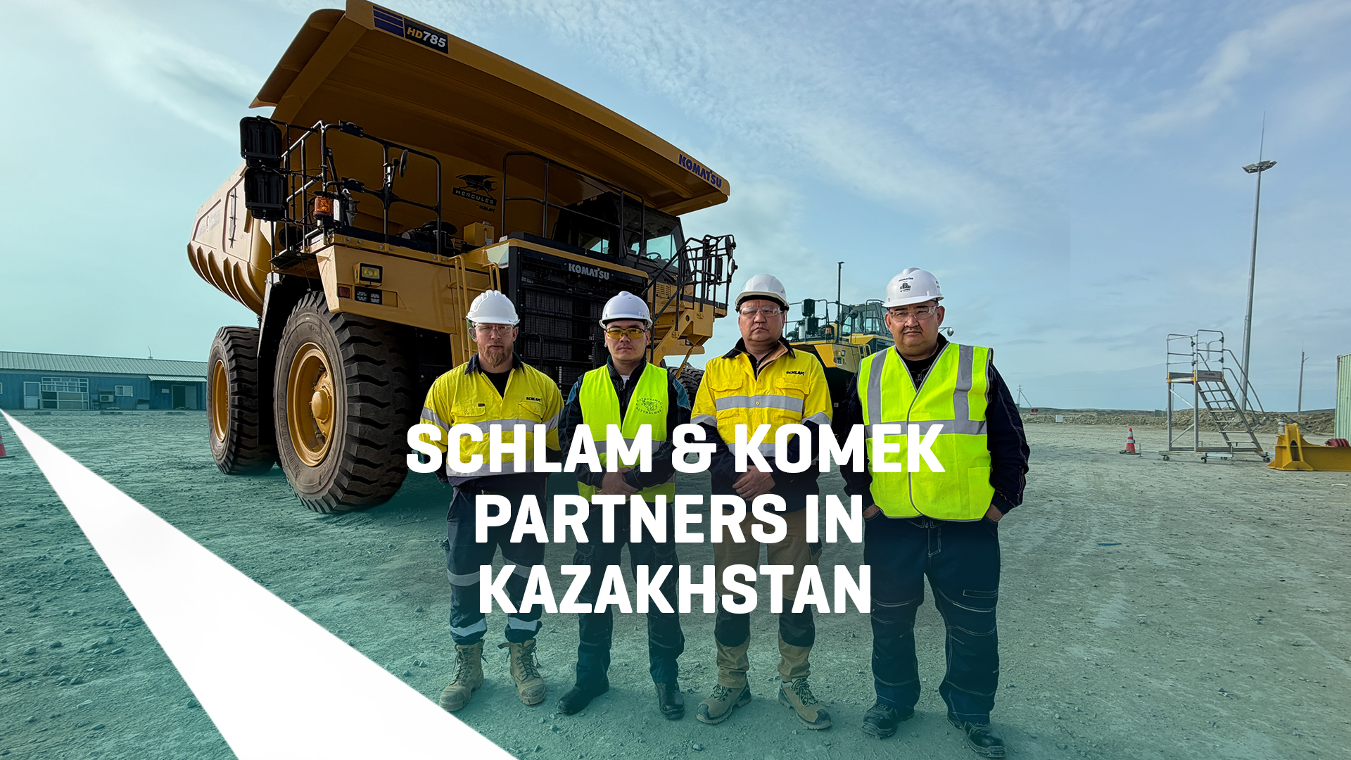 "Four workers in high-vis vests and hard hats stand in front of a Komatsu HD785 haul truck fitted with a Schlam Hercules truck bed at a mine site in Kazakhstan."