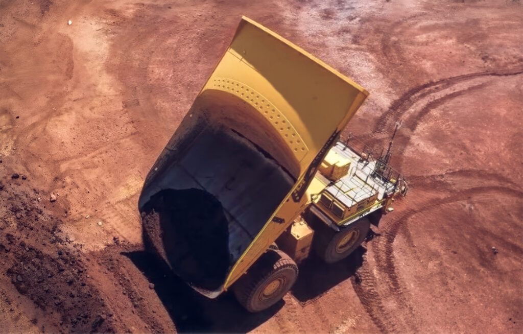 Aerial view of a mining haul truck dumping its load, with material still clinging to the bed after the dump cycle, illustrating carry back.